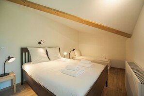 Une chambre avec un grand lit, deux tables de chevet avec des lampes, un radiateur et des poutres en bois au plafond.