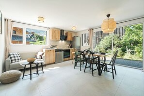 Eine moderne Küche mit Holzausbau, einem Essbereich mit Stühlen und einem großen Fenster mit Blick auf Grünflächen.
