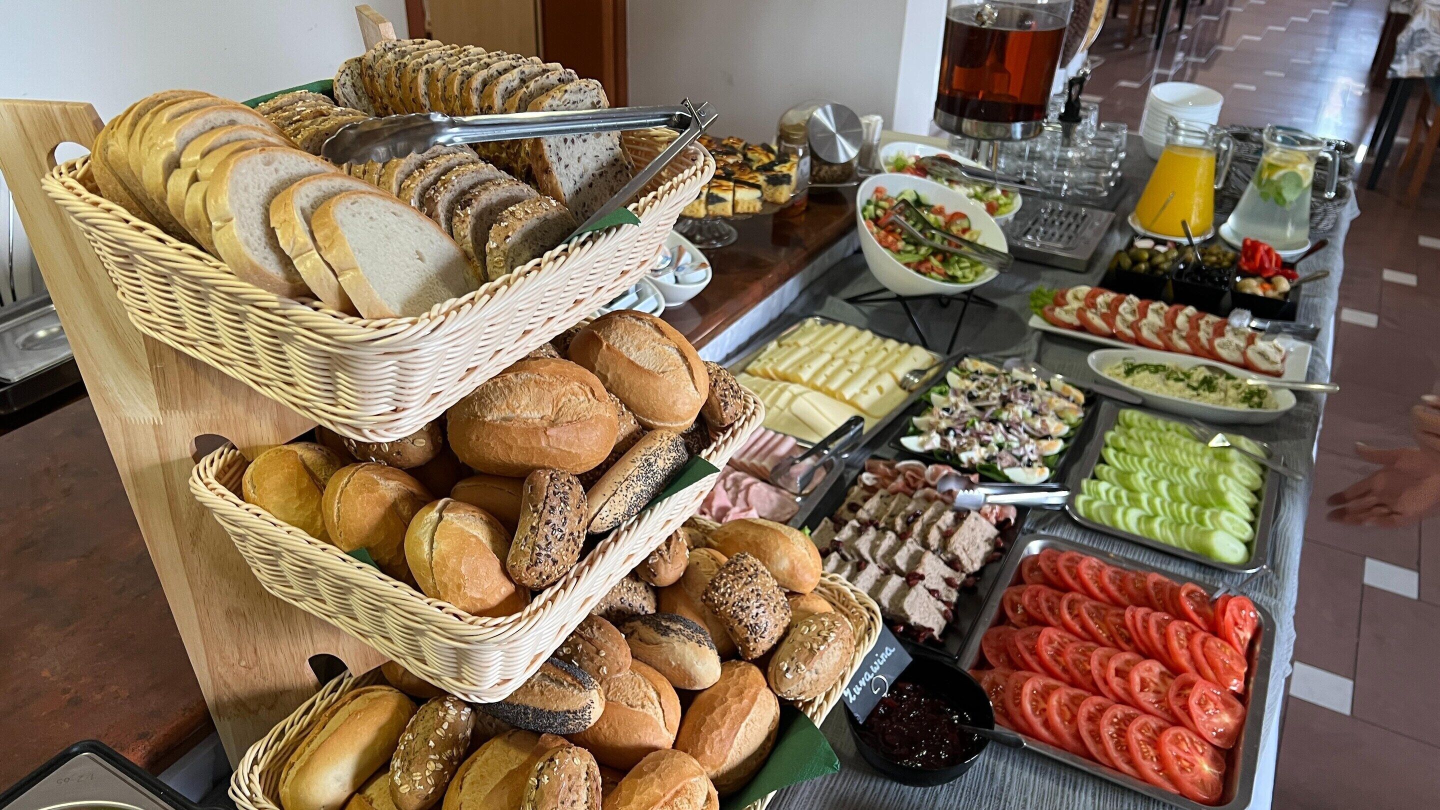 A buffet with various breads, cheeses, meats, and salads.