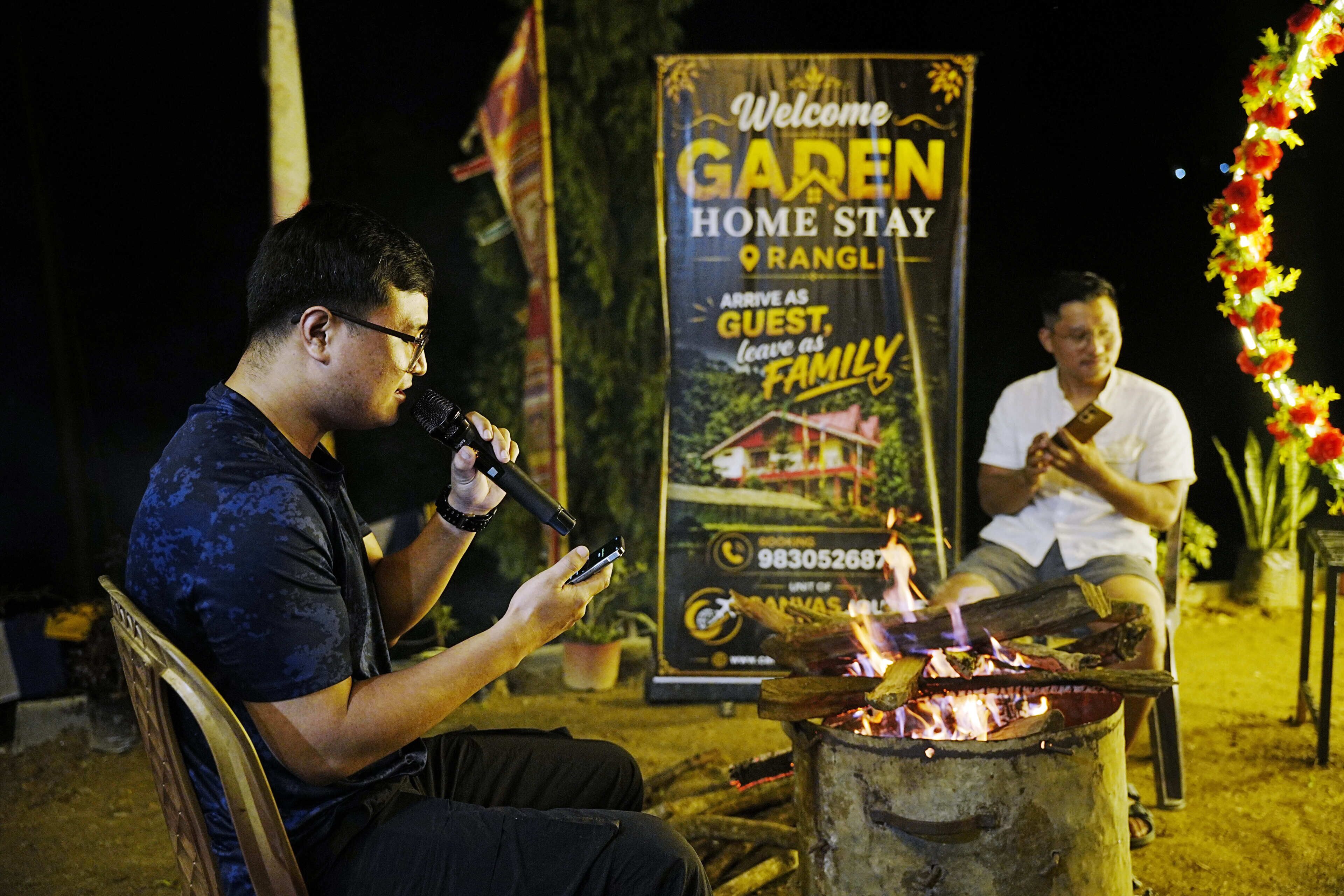 A person speaking into a microphone with a sign in the background advertising a home stay.