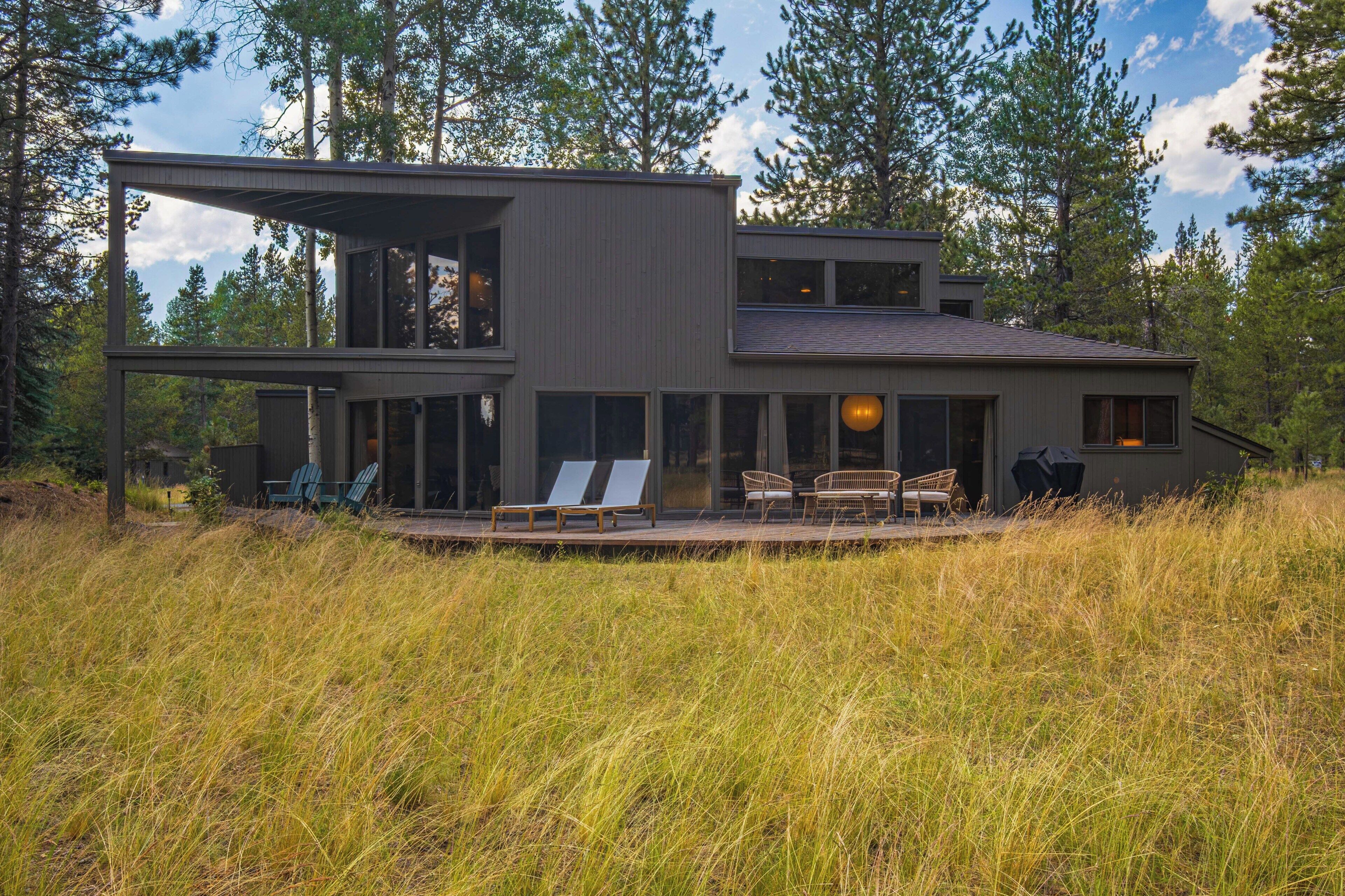 Et moderne hus med to etager, en terrasse, store vinduer og udendørs siddepladser.