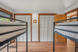A room with bunk beds, a wooden floor, and a door with louvered shutters. - Mid Century Modern with Sweeping Golf View (Sunriver)