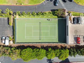 Vista aérea de una cancha de tenis con plazas de estacionamiento y una carretera adyacente.
