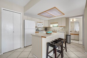 A modern kitchen with a central island, white cabinetry, a microwave, and a coffee maker. - South Maui Beach Getaway | 2BR Condo Across from Kamaole Beach II (Kihei)