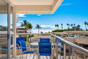 A balcony with a view of the ocean, palm trees, and a parking area. - South Maui Beach Getaway | 2BR Condo Across from Kamaole Beach II (Kihei)