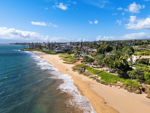 A coastal view with a sandy beach, ocean waves, and a residential area with houses and greenery. - South Maui Beach Getaway | 2BR Condo Across from Kamaole Beach II (Kihei)