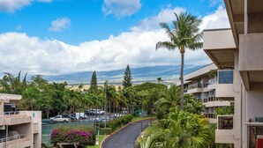 A residential area with a curved road, palm trees, and a view of distant mountains. - South Maui Beach Getaway | 2BR Condo Across from Kamaole Beach II (Kihei)