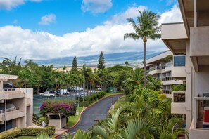 A residential area with a curved road, palm trees, and a view of distant mountains. - South Maui Beach Getaway | 2BR Condo Across from Kamaole Beach II (Kihei)
