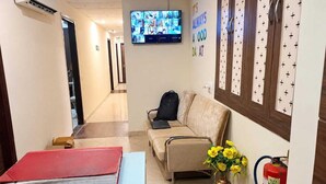 A hotel lobby with a reception desk, a sofa, a television displaying multiple screens, and a fire extinguisher. - Classic Hotel Elegant Palace (New Delhi)