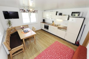 Cocina compacta con comedor, televisor en la pared y microondas en la encimera.