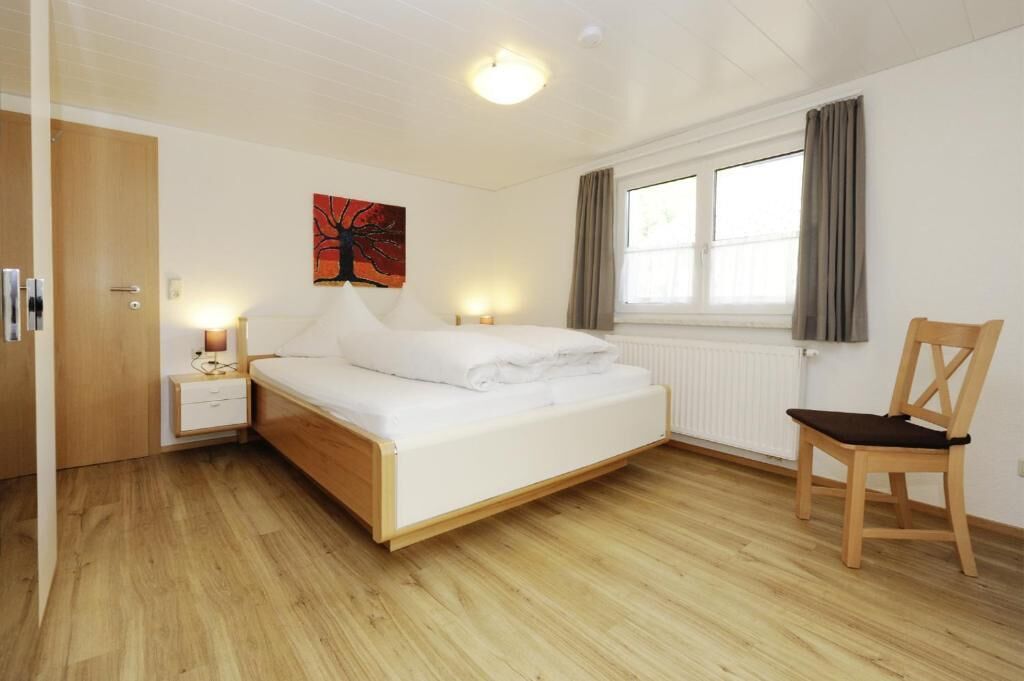 A bedroom with a bed, bedside tables, a chair, a window, and a painting on the wall.