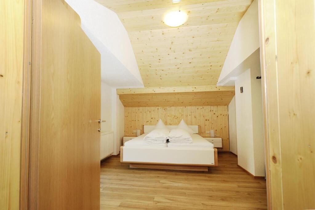 Een slaapkamer met een houten plafond, een bed met wit beddengoed en een houten vloer.