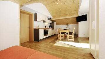 A compact kitchen with modern appliances, a dining area with a table and chairs, and a wooden ceiling.