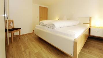 Ein Zimmer mit einem Einzelbett, Holzboden, einem Holzstuhl, einem Nachttisch mit Lampe und einer Tür.