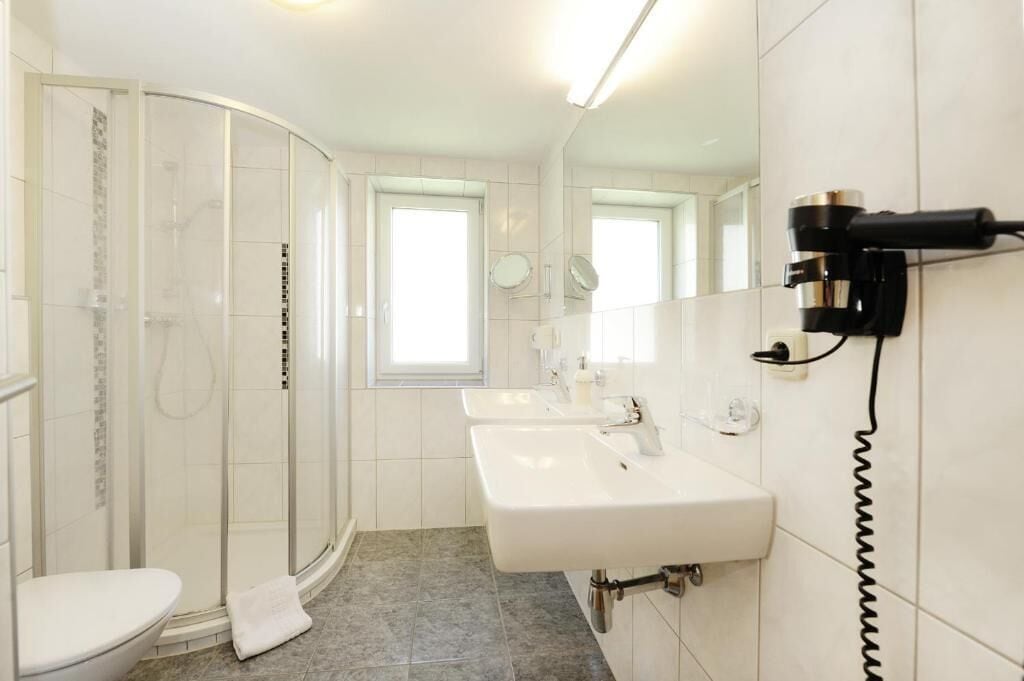 Un bagno moderno con doccia vetrata, due lavandini e un asciugacapelli fissato al muro.