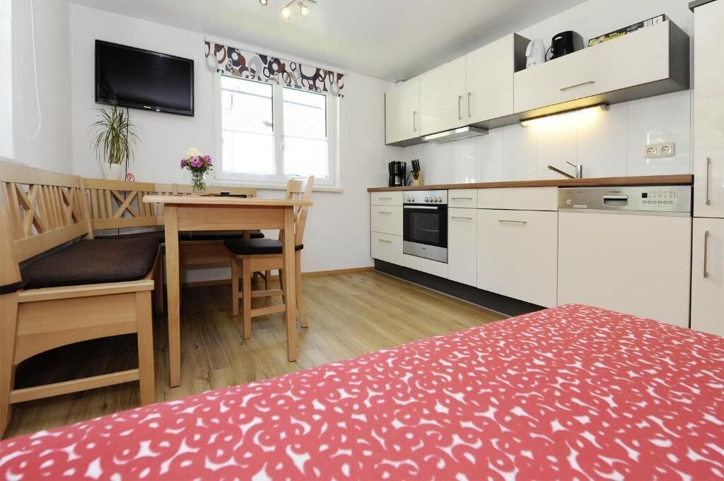 A compact room with a bed, a dining table, a TV, a kitchenette, and a window.