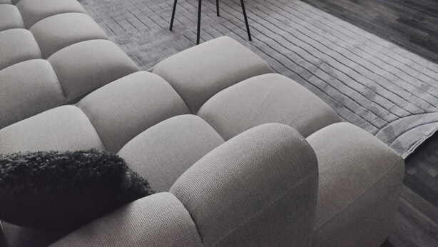 A modern bedroom with a bed, a sofa, a small table, and a potted plant.