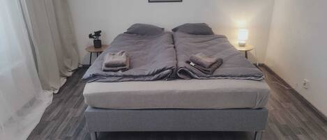 A double bed with grey bedding, a bedside table with a lamp, and a framed picture on the wall.