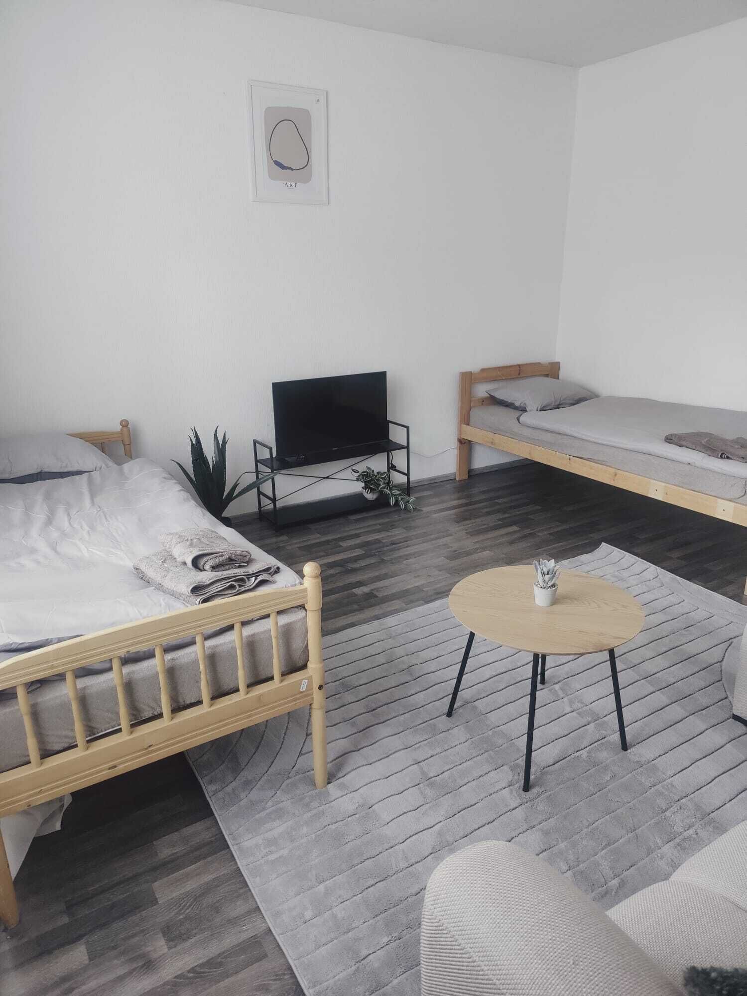 A room with two beds, a TV on a stand, a round table, and a grey patterned rug.