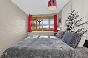 A bedroom with a bed, a window with curtains, a lamp, and a wall-mounted artwork.