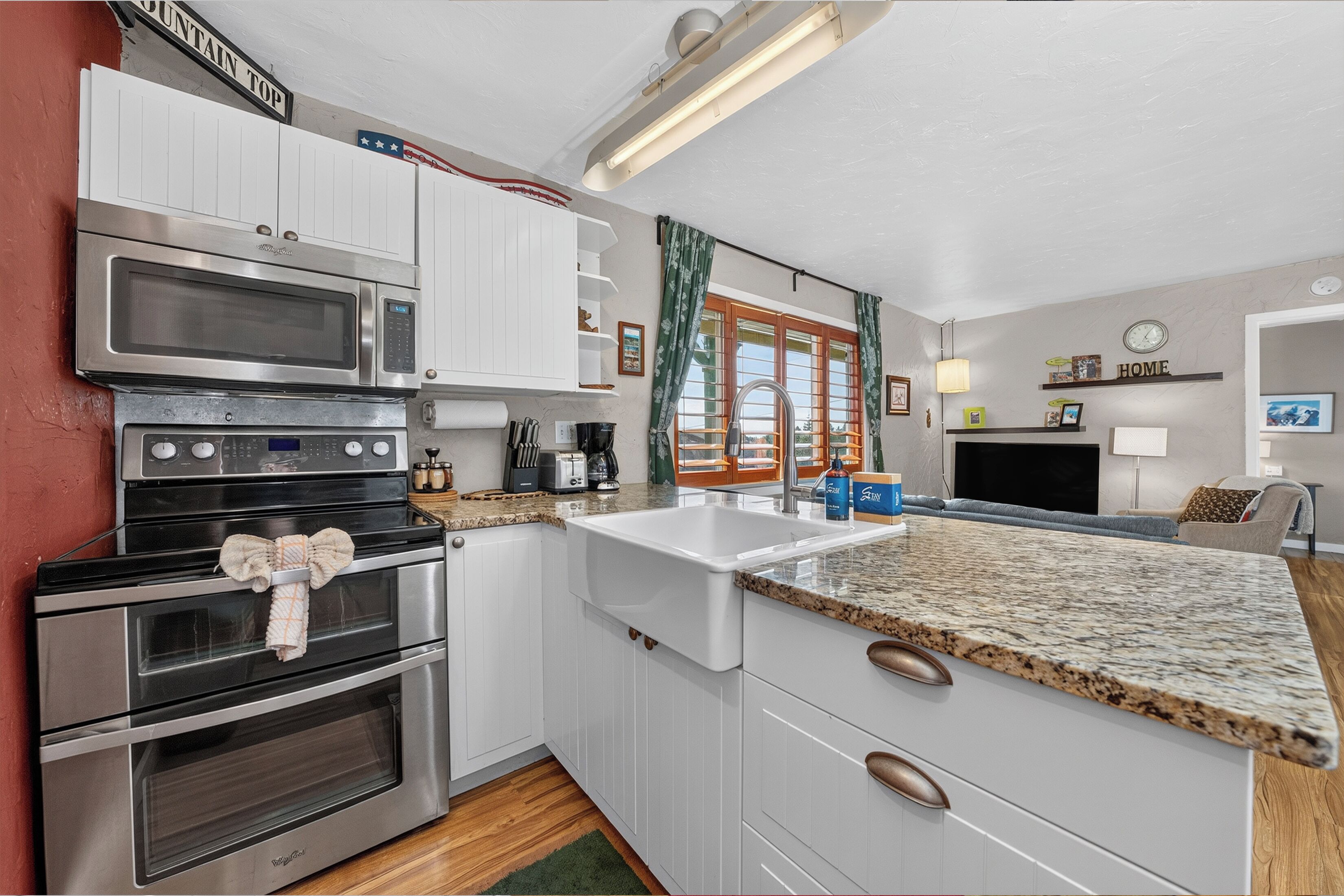 A kitchen with white cabinets, stainless steel appliances, a granite countertop, and a window with curtains.