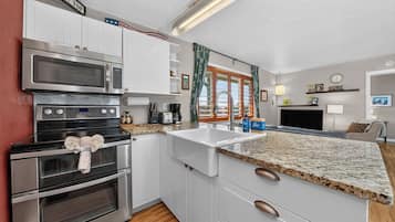 A kitchen with white cabinets, stainless steel appliances, a granite countertop, and a window with curtains.