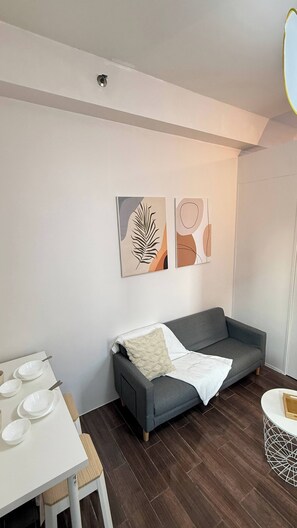 A modern living room with a grey sofa, a white table with plates, and abstract wall art. - Central Makati Place With Queen bed and 55 Inch Smart TV (Makati)