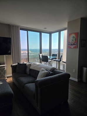 A living room with a sofa, a TV, a balcony with a table and chairs, and a painting on the wall. - Stunning Arlington Condo with Balcony & Views Near Pentagon City (Arlington)