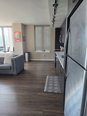 A modern living room with a sofa, a dining table, and a kitchen area with a refrigerator and cabinets. - Stunning Arlington Condo with Balcony & Views Near Pentagon City (Arlington)