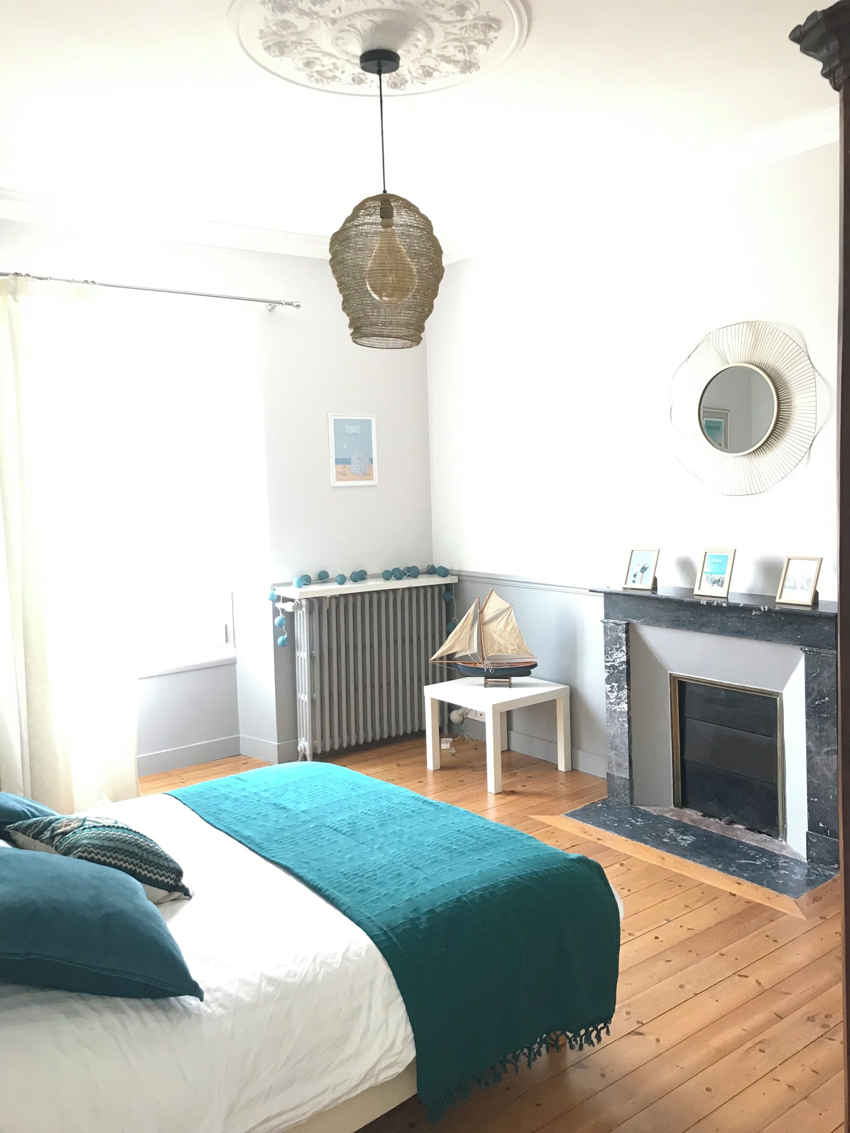 A bedroom with a bed, a small table with a sailboat model, a fireplace, and a radiator.