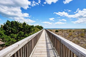 A wooden boardwalk leading to a beach with green vegetation on one side and a clear blue sky. - Updated oceanfront 3br/3bath condo at Wrightsville Dunes! (Wrightsville Beach)