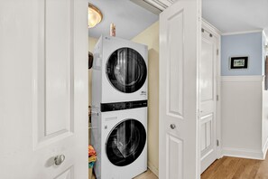 Une buanderie équipée d’un lave-linge et d’un sèche-linge à chargement frontal, d’une porte avec une poignée et d’un luminaire au plafond.
