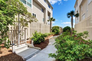 A residential building with a covered walkway, palm trees, and a wooden fence. - Updated oceanfront 3br/3bath condo at Wrightsville Dunes! (Wrightsville Beach)