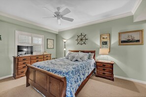 Une chambre  à coucher avec un lit en bois, un ventilateur de plafond, une table de chevet, une lampe et un gouvernail de bateau fixé au mur.