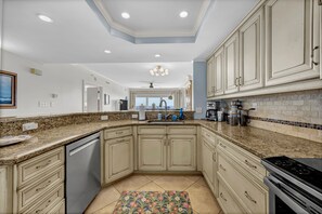 A modern kitchen with granite countertops, white cabinetry, and a large island. - Updated oceanfront 3br/3bath condo at Wrightsville Dunes! (Wrightsville Beach)