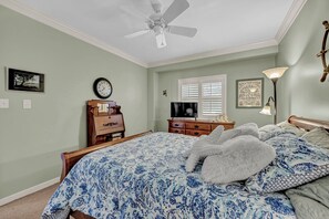 Een slaapkamer met een bed, een plafondventilator, een dressoir, een televisie en een ingelijst schilderij aan de muur.