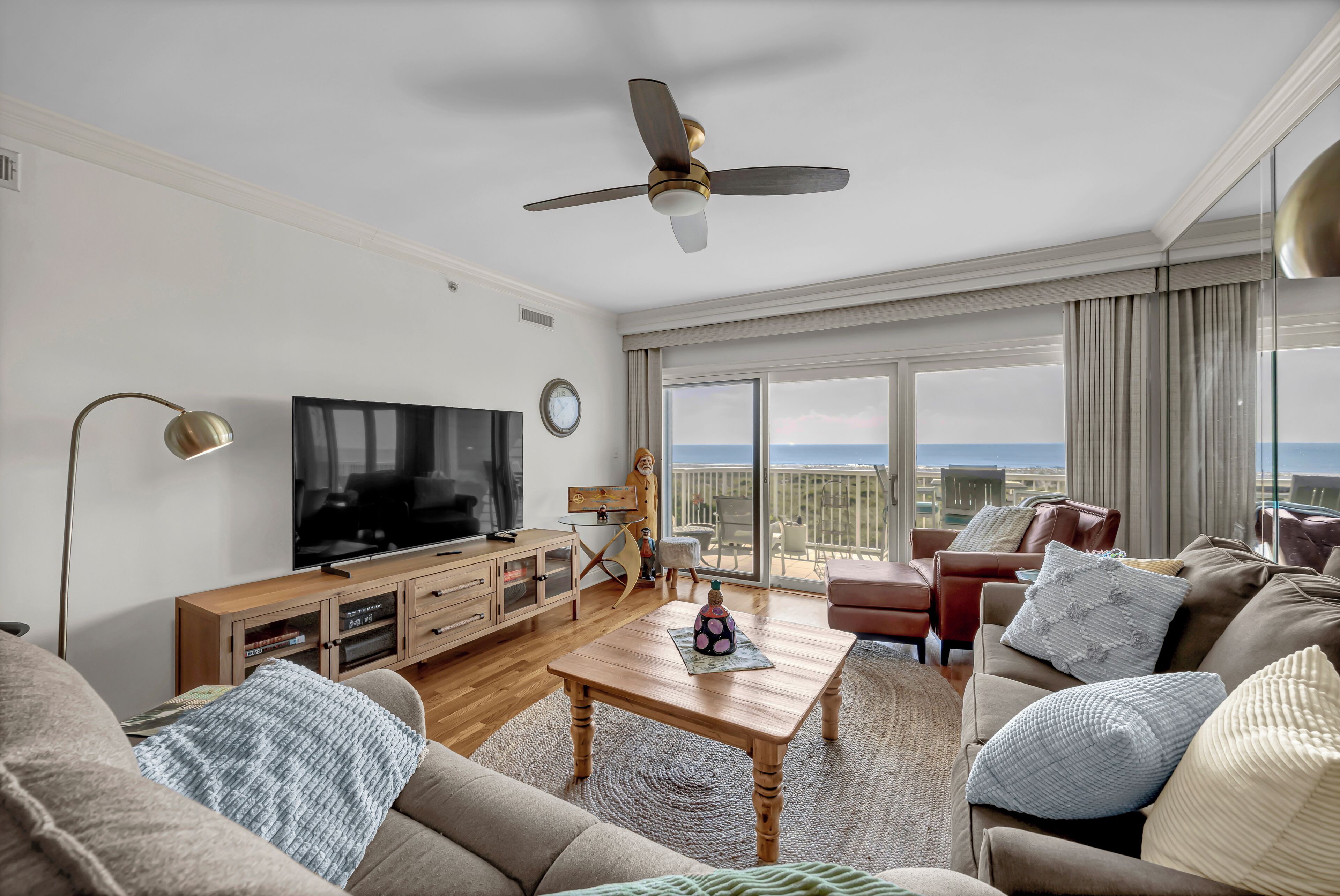 A modern living room with a flat-screen TV, wooden furniture, a ceiling fan, and a large window with a view.