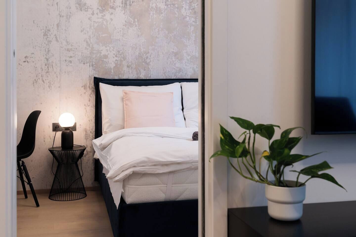 Een moderne slaapkamer met een bed, bedlamp, stoel en een potplant.