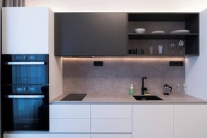A modern kitchen with built-in ovens, a countertop with a sink, and a shelf with glassware. - Urban Oasis Brno - I (Brno-město)