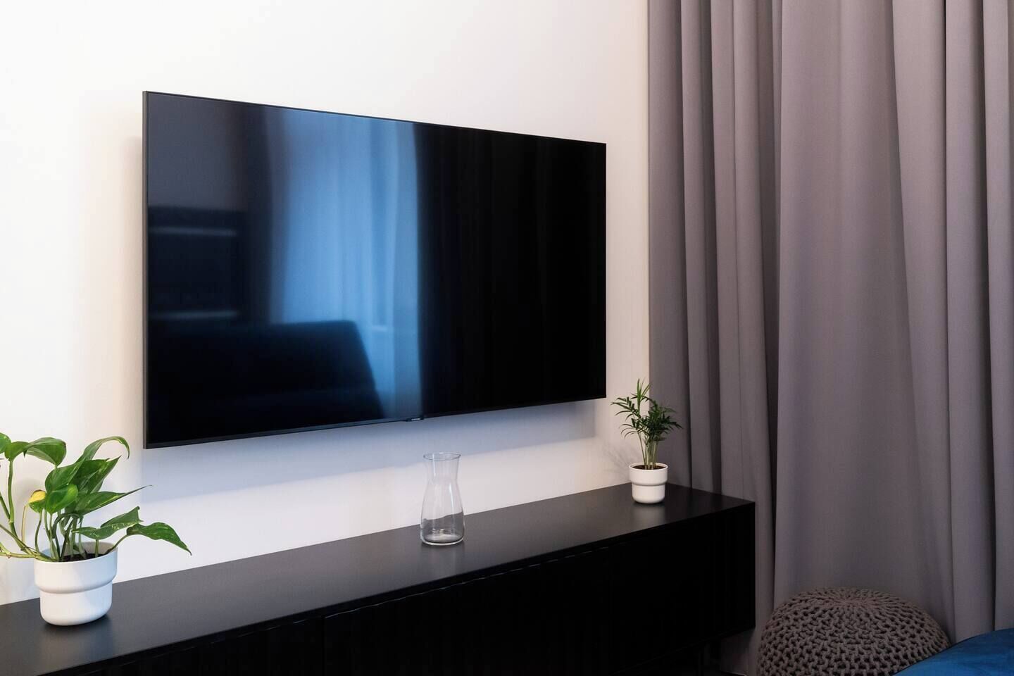 A modern living room with a flat-screen TV mounted on a black console, a potted plant, and a glass vase.