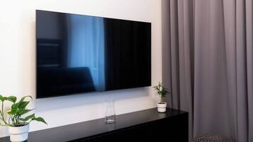 A modern living room with a flat-screen TV mounted on a black console, a potted plant, and a glass vase.