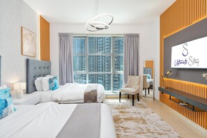 A hotel room with a large bed, a chair, a desk, a mirror, and a view of high-rise buildings. - bnbme - Stand Point A - 2BR (Dubai)