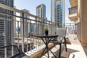 A balcony with a table and chairs, overlooking a cityscape with high-rise buildings. - bnbme - Stand Point A - 2BR (Dubai)