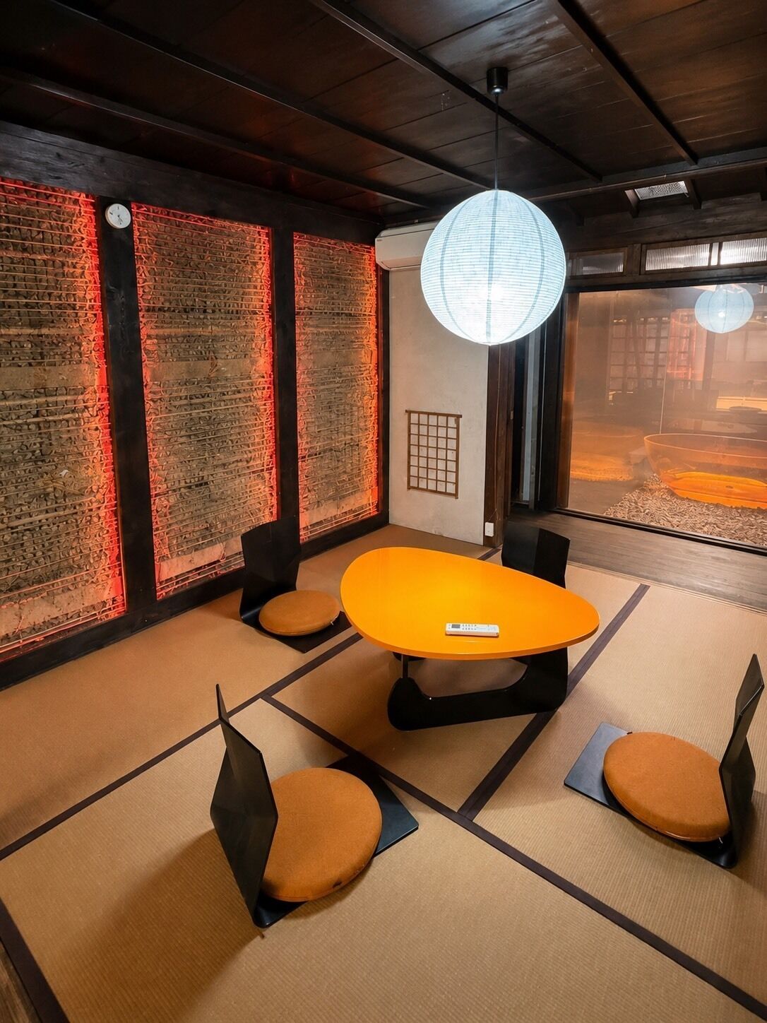 Quarto com piso de tatame, uma mesa central, cadeiras, um relógio e uma janela grande com vista.