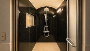 Un baño moderno con ducha de vidrio, paredes de mármol y piso en tonos neutros.