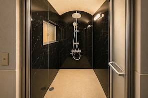Ein modernes Badezimmer mit einer gläsernen Dusche, Marmorwänden und einem Boden in neutralen Tönen.