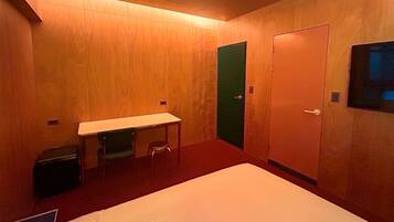 Habitación de hotel con cama, escritorio, dos sillas, un cesto de basura y una puerta.