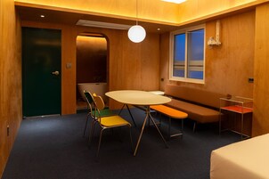 Habitación de hotel con decoración de madera, una mesa redonda con sillas, un banco, una ventana con persianas y una puerta.