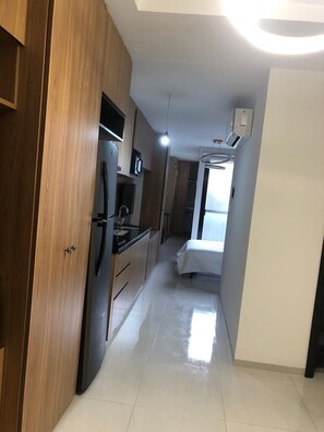 Un pasillo estrecho con armarios de madera, un refrigerador y una cama con cubrecama blanco.