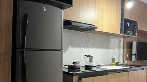 Una cocina moderna con un refrigerador de acero inoxidable, armarios de madera, un microondas y una encimera negra.